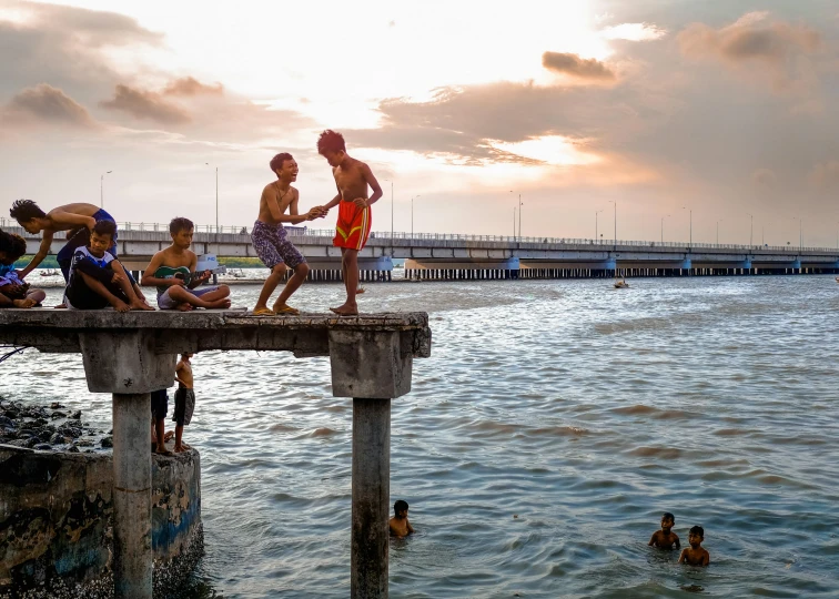 a group of people standing on top of a pier, by Joze Ciuha, pexels contest winner, happening, kids playing, indonesia national geographic, late afternoon, people swimming