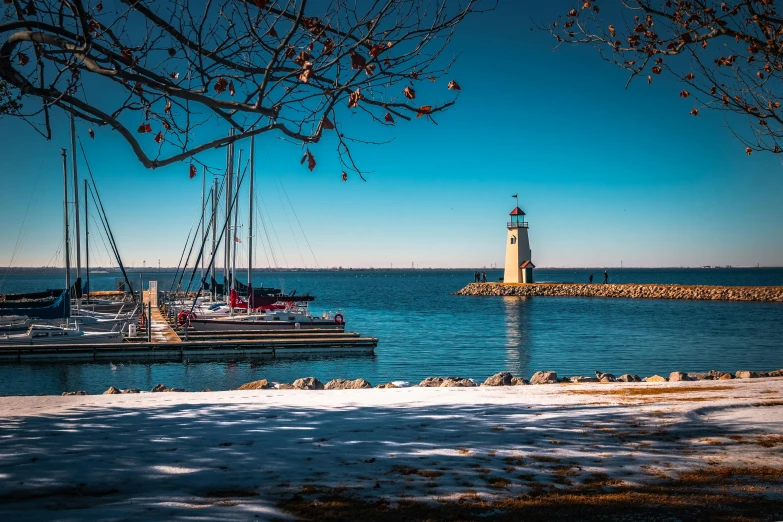 a large body of water with a light house in the background, by Ryan Pancoast, pexels contest winner, sunny winter day, sailboats, from wheaton illinois, harbour