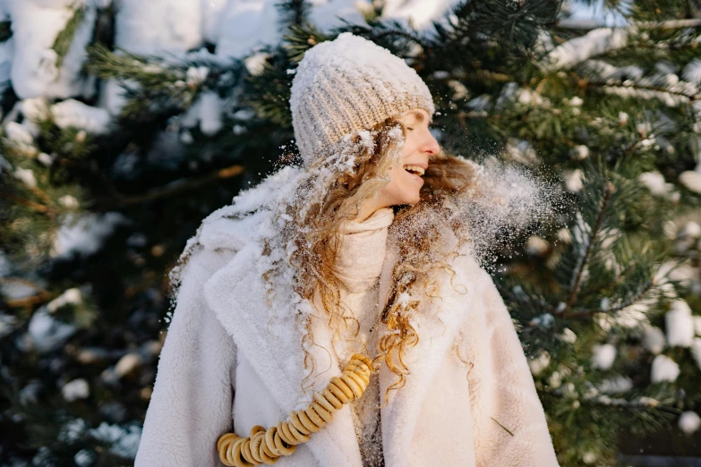 a woman standing in front of a tree covered in snow, trending on pexels, long blond drill curls, covered in white flour, gif, warm color clothes