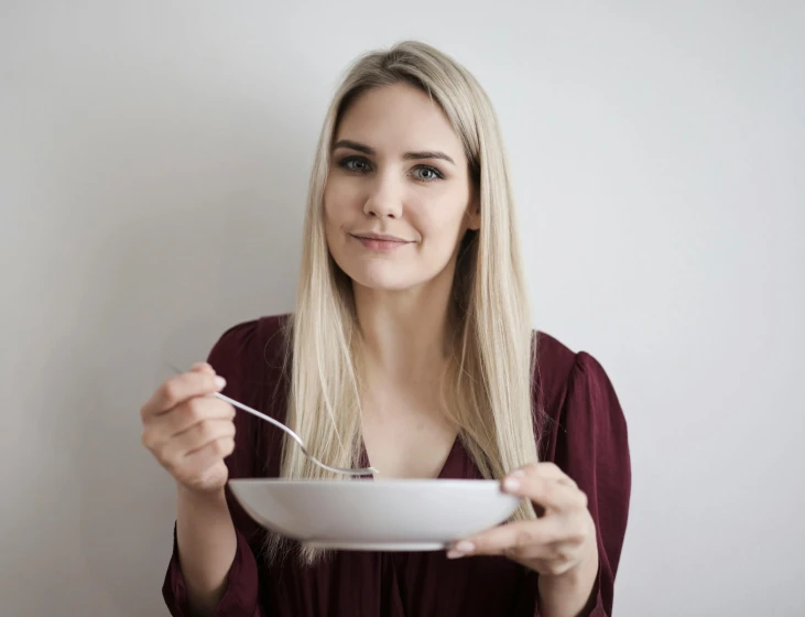 a woman holding a bowl with a spoon in it, inspired by Louisa Matthíasdóttir, pexels contest winner, blonde beautiful young woman, plain background, people inside eating meals, rectangle