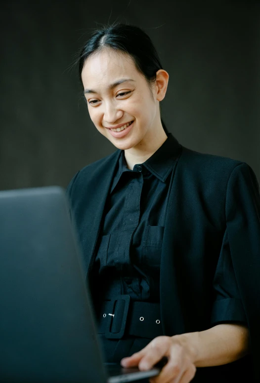 a woman sitting in front of a laptop computer, inspired by Ruth Jên, trending on pexels, wearing a black noble suit, smiling young woman, androgynous person, indonesia