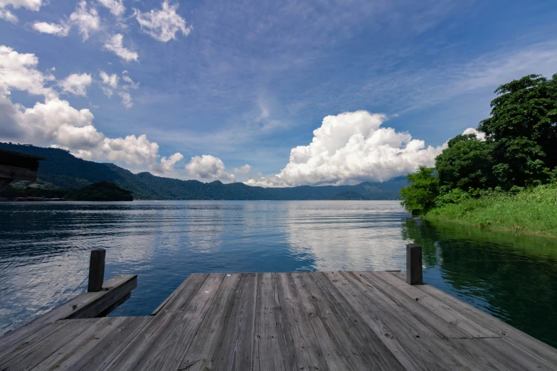 a dock on a lake with mountains in the background, inspired by Tadao Ando, pexels contest winner, sumatraism, clear blue skies, peaceful cloud, tochigi prefecture, lush scenery