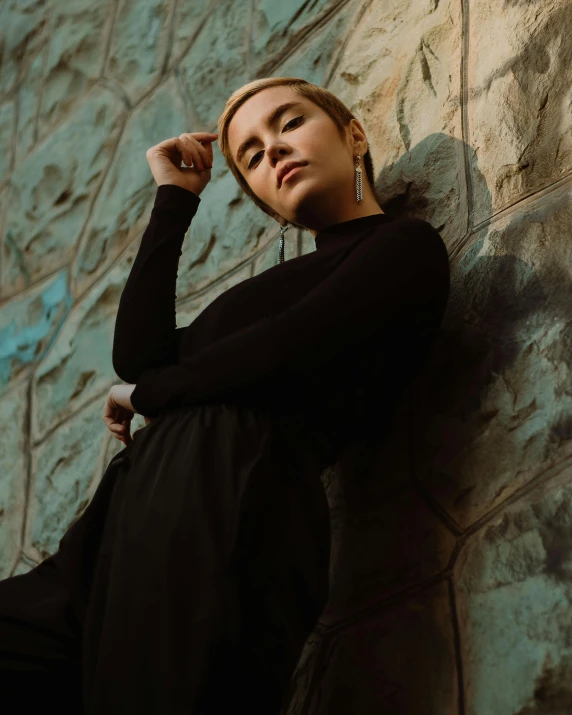 a woman in a black dress leaning against a stone wall, inspired by Elsa Bleda, pexels contest winner, non-binary, portrait image, sydney sweeney, an asian woman