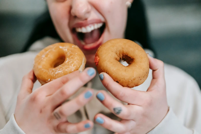 a close up of a person holding two doughnuts, by Nicolette Macnamara, pexels contest winner, excited, 🦩🪐🐞👩🏻🦳, woman, extra greasy