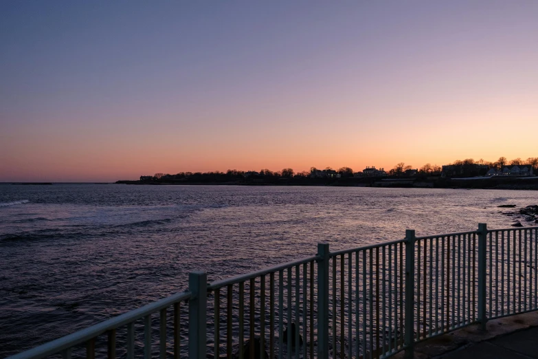 a fence that is next to a body of water, unsplash, vista of a city at sunset, new jersey, 2022 photograph, sunset + hdri