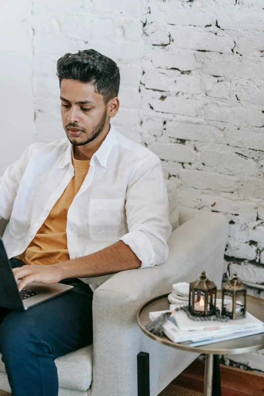 a man sitting on a couch using a laptop, trending on pexels, renaissance, middle eastern style vendors, wearing a white shirt, androgynous person, peruvian looking