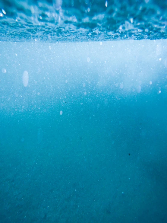 an underwater view of a body of water, bubbles rising, at the bottom of the ocean, surf photography, half blue