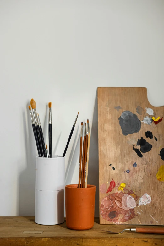 a painting board sitting on top of a wooden table, trending on pexels, academic art, holding paintbrushes, white wall coloured workshop, still life photo of a backdrop, paint tubes