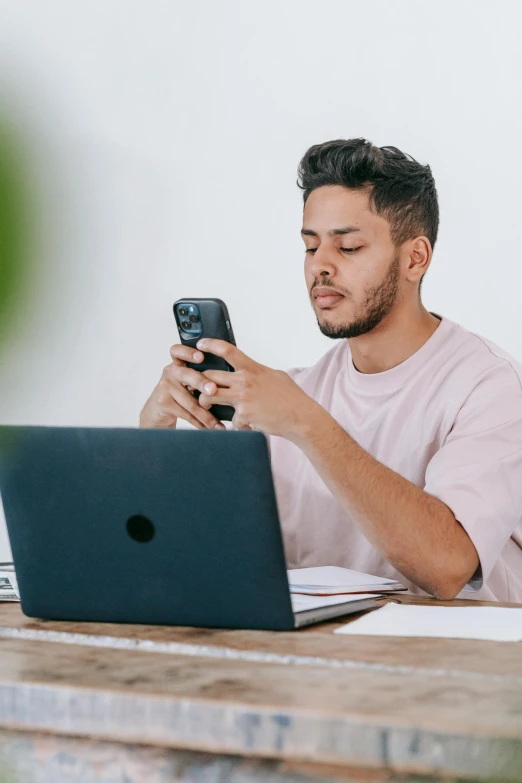 a man sitting at a table with a laptop and a cell phone, by Adam Rex, trending on pexels, plain background, lgbtq, instagram post, studious