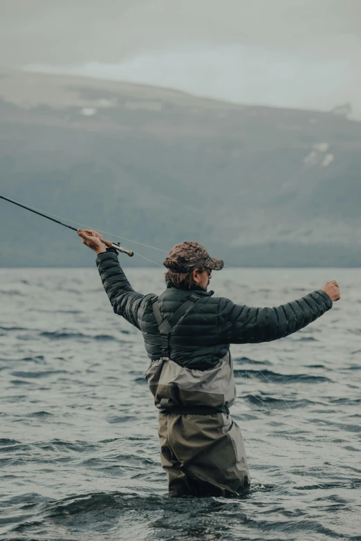 a man that is standing in the water with a fish, dabbing, patagonian, wearing adventure gear, fly
