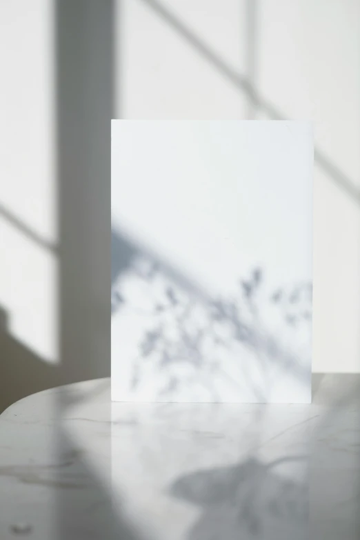 a card sitting on top of a table next to a window, a picture, by Leo Leuppi, postminimalism, white background with shadows, soft sunbeam, detailed product image, silhouette