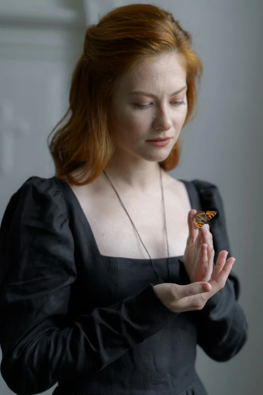 a woman in a black dress holding a butterfly, inspired by Lucas Cranach the Elder, unsplash, eleanor tomlinson, doing a prayer, karen gillan, taken in the late 2010s