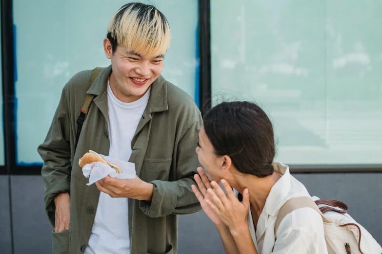 a man standing next to a woman eating a hot dog, pexels contest winner, young cute wan asian face, greeting hand on head, non-binary, laughing out loud