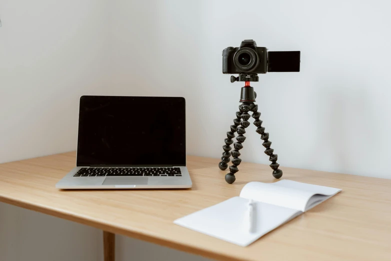 a laptop computer sitting on top of a wooden desk, unsplash, video art, tripod, set against a white background, waving at the camera, high quality photo