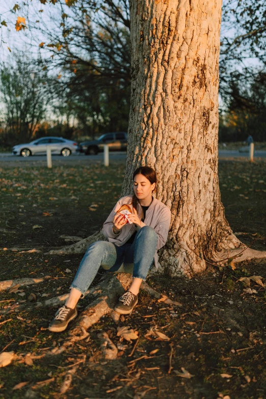 a woman sitting under a tree eating a donut, an album cover, by Andrew Stevovich, pexels contest winner, soft evening lighting, joey king, cuddling her gremlings, cinestill 800t 35mm eastmancolor