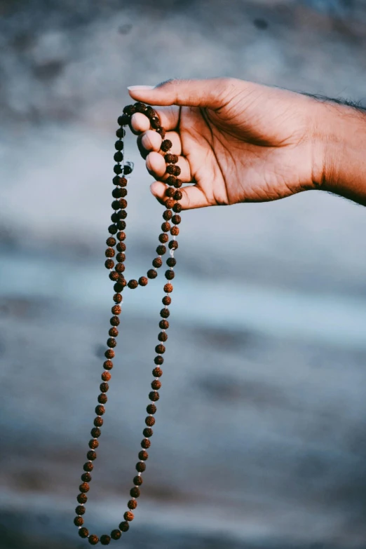 a person holding a rosary in their hand, unsplash, sri lanka, black and brown colors, instagram post, indigo