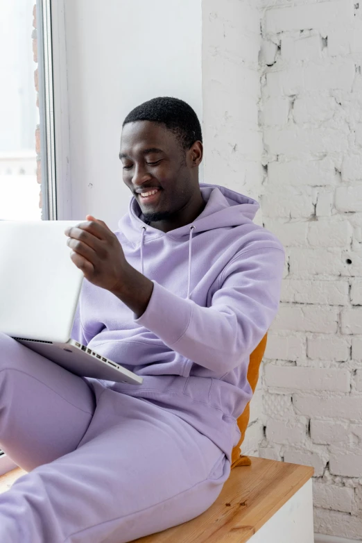 a man sitting on a chair using a laptop, trending on pexels, happening, wearing a purple sweatsuit, black man, pastel clothing, an all white human