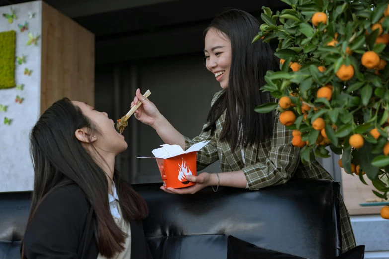 a couple of women standing next to each other eating food, inspired by Wang Duo, pexels contest winner, orange and white, young asian girl, serving fries, promotional image
