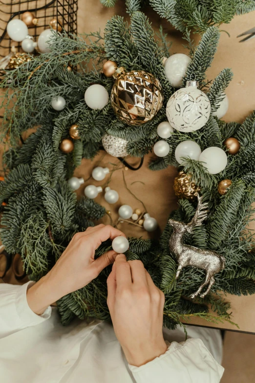 a woman decorating a christmas wreath with ornaments, by Julia Pishtar, professionally assembled, elegant light, cardboard, cozy