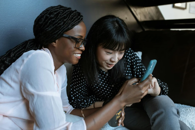 two women sitting on a couch looking at a cell phone, trending on pexels, diverse, schools, avatar image, asian girl