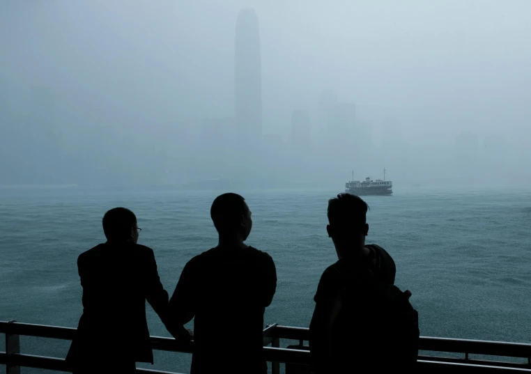 a group of people standing next to a body of water, a picture, inspired by Zhang Kechun, pexels contest winner, romanticism, city fog, silhouette, looking out over the sea, hong kong