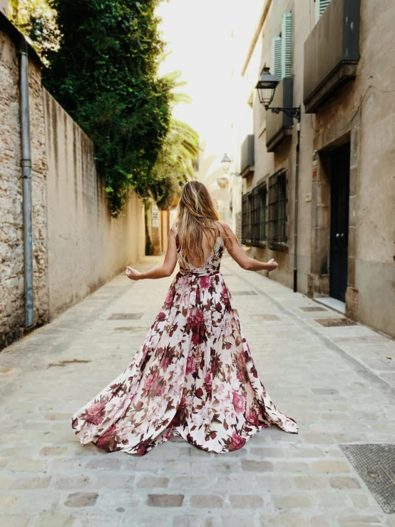 a woman in a long dress walking down a street, by Sara Saftleven, unsplash, happening, wearing pink floral gown, back slit, al fresco, luxury dress