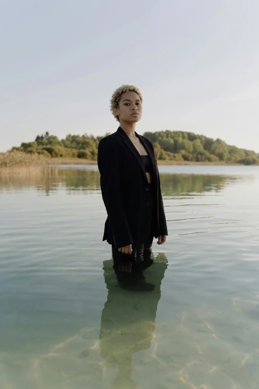 a woman standing in a body of water, an album cover, pexels, wearing a black suit, light skin, non binary model, concern