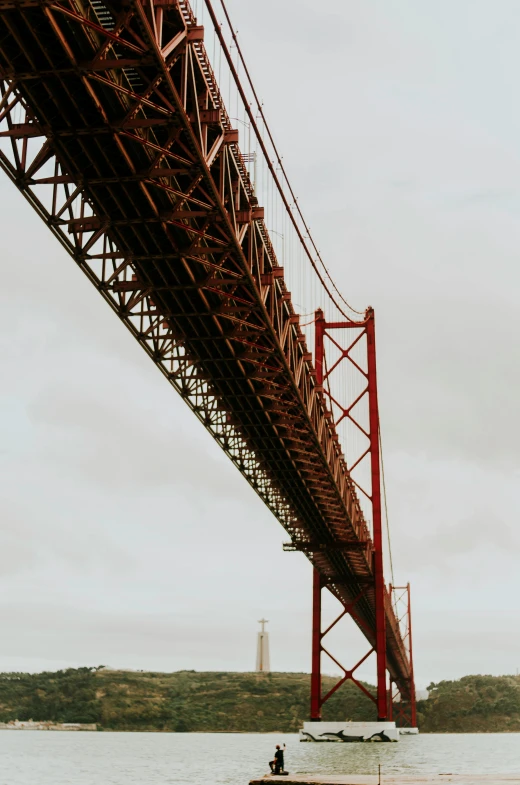 a boat in a body of water under a bridge, a red cape, view from bottom to top, ponte 2 5 de abril, high-quality photo