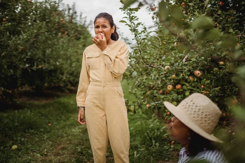 a woman standing next to a boy in an apple orchard, pexels contest winner, wearing human air force jumpsuit, beige, “zendaya, wearing honey