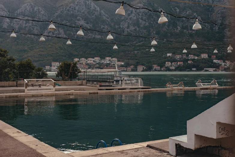 a view of a body of water with mountains in the background, by Elsa Bleda, unsplash contest winner, modernism, mediterranean fisher village, floating lights, croatian coastline, next to a pool