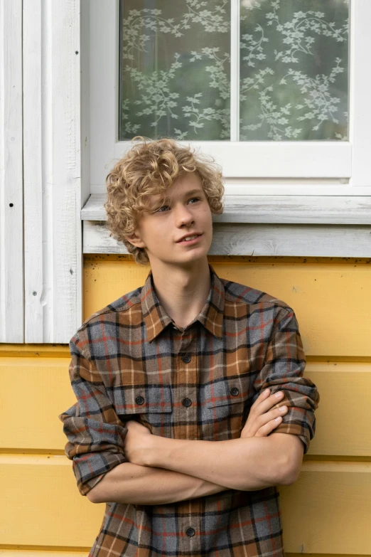 a young man leaning against a yellow wall, an album cover, by Jacob Toorenvliet, trending on pexels, renaissance, pale skin curly blond hair, wearing plaid shirt, finland, standing near a window