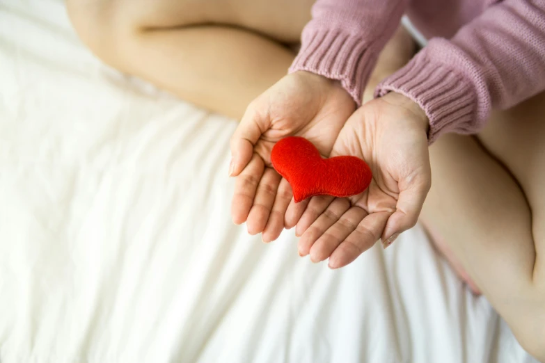 a woman holding a red heart in her hands, a photo, trending on pexels, small bed not made, soft pads, holding hand, health supporter