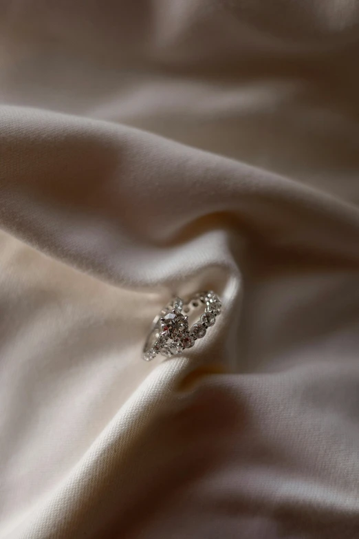 a close up of a wedding dress on a bed, by Jessie Algie, platinum jewellery, close up of single sugar crystal, shaped like torus ring, shot with sony alpha 1 camera