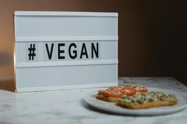 a plate of pizza next to a sign that says vegan, a picture, by Julia Pishtar, trending on unsplash, light box, on grey background, led display, white box