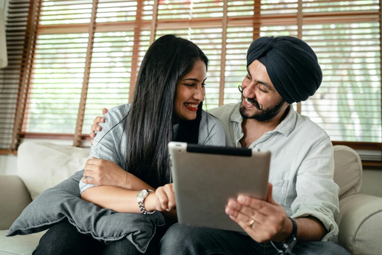 a man and woman sitting on a couch looking at a tablet, inspired by Manjit Bawa, australian, happy couple, profile image, thumbnail