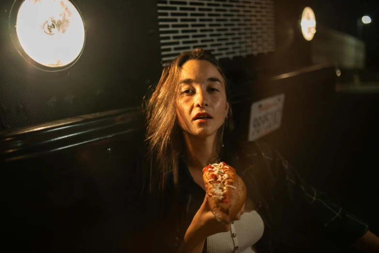 a woman eating a donut in a dark room, a portrait, by Julia Pishtar, pexels contest winner, korean woman, holding pizza, hot dog, lights inside