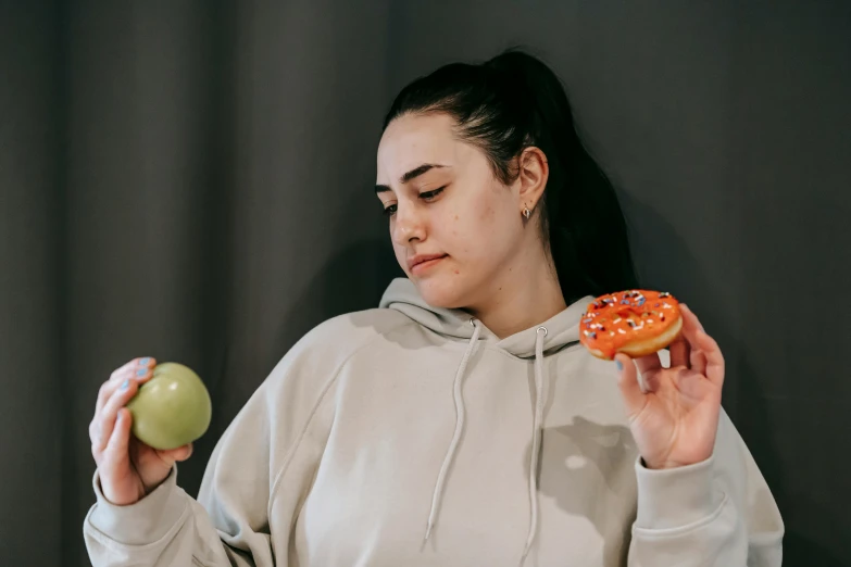 a woman holding an apple and a donut, by Julia Pishtar, trending on pexels, wearing a tracksuit, concerned, profile image, sydney hanson