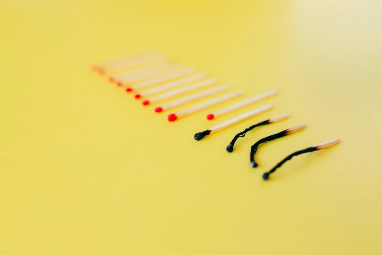 a row of matches sitting on top of a table, pexels, minimalism, black and yellow and red scheme, acupuncture treatment, on a yellow canva, burn