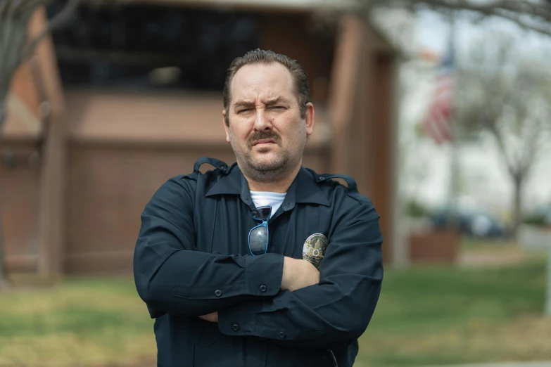 a man standing in front of a building with his arms crossed, a portrait, by Winona Nelson, unsplash, wearing a police uniform, dan harmon, sam hyde, portrait shot 8 k