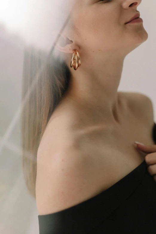 a woman wearing a black top and gold earrings, a picture, by Emma Andijewska, trending on pexels, made of polished broze, side - view, rose gold, julia sarda