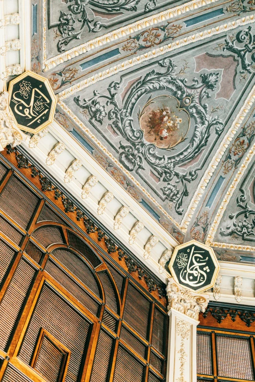 a clock mounted to the ceiling of a building, an album cover, inspired by Osman Hamdi Bey, trending on unsplash, baroque, inhabited initials, intricate detailed roof, interior of a library, caligraphy