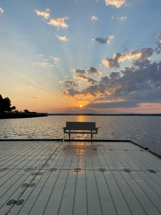 a bench sitting on top of a wooden dock, during a sunset, in the center of the image, tyndall rays, sitting down