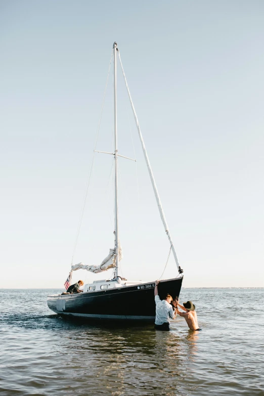 a man standing in the water next to a boat, by Winona Nelson, minimalism, with anchor man and woman, playful pose, bay area, standing on the mast