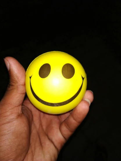 a person holding a smiley face ball in their hand, a picture, pexels, happening, ( ( dark skin ) ), wide forehead, yellow, emote