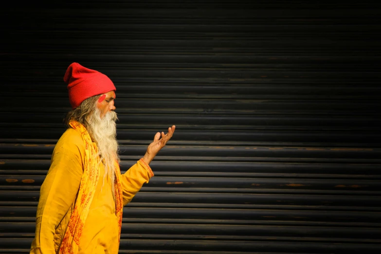 a man with a long white beard and a red hat, an album cover, inspired by Steve McCurry, pexels contest winner, street art, anjali mudra, yellow robes, nostalgic 8k, emanating magic from her palms
