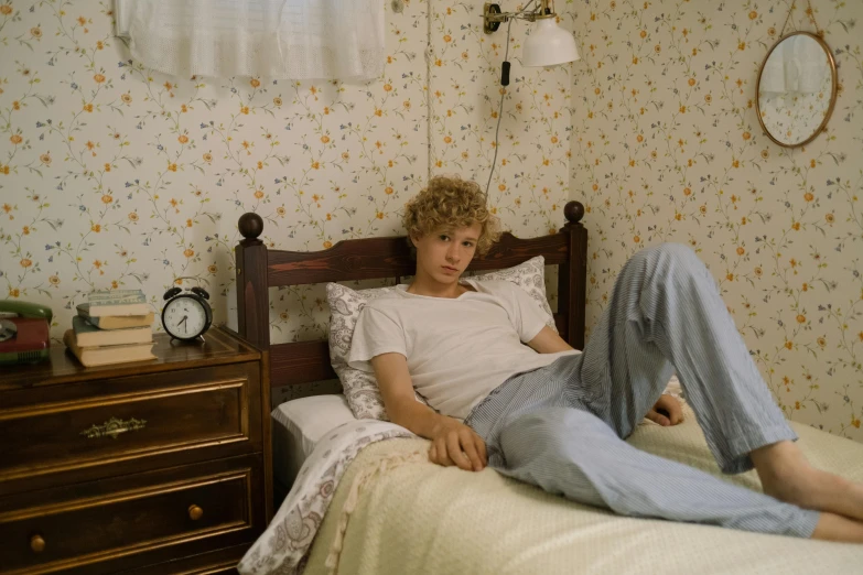 a man laying on top of a bed next to a dresser, an album cover, pale skin curly blond hair, movie still 8 k, male teenager, midsummer