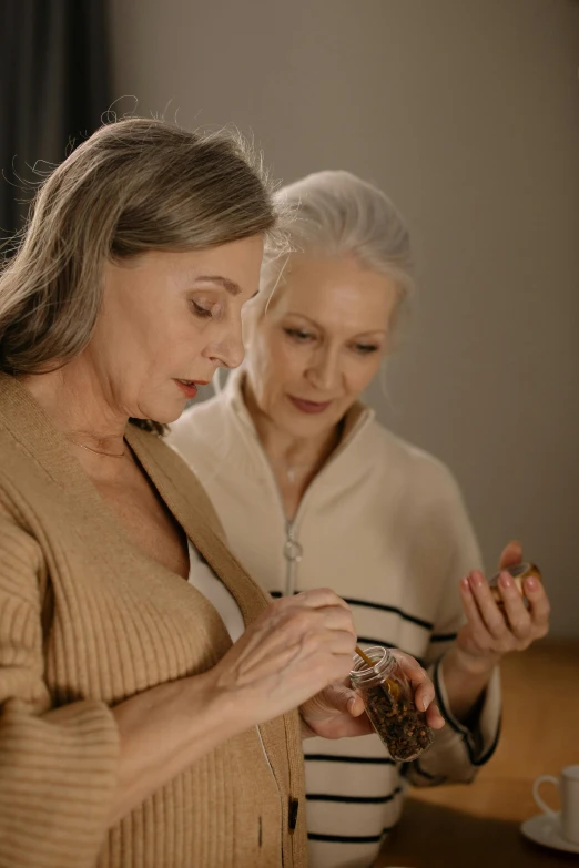 a couple of women standing next to each other, a picture, trending on pexels, carrying a bottle of perfume, gray haired, inspect in inventory image, brown
