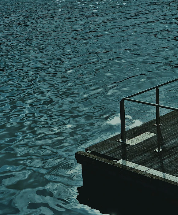 a man sitting on top of a wooden dock next to a body of water, an album cover, inspired by Elsa Bleda, unsplash, postminimalism, pool caustics, photo of zurich, dark. no text, railing along the canal