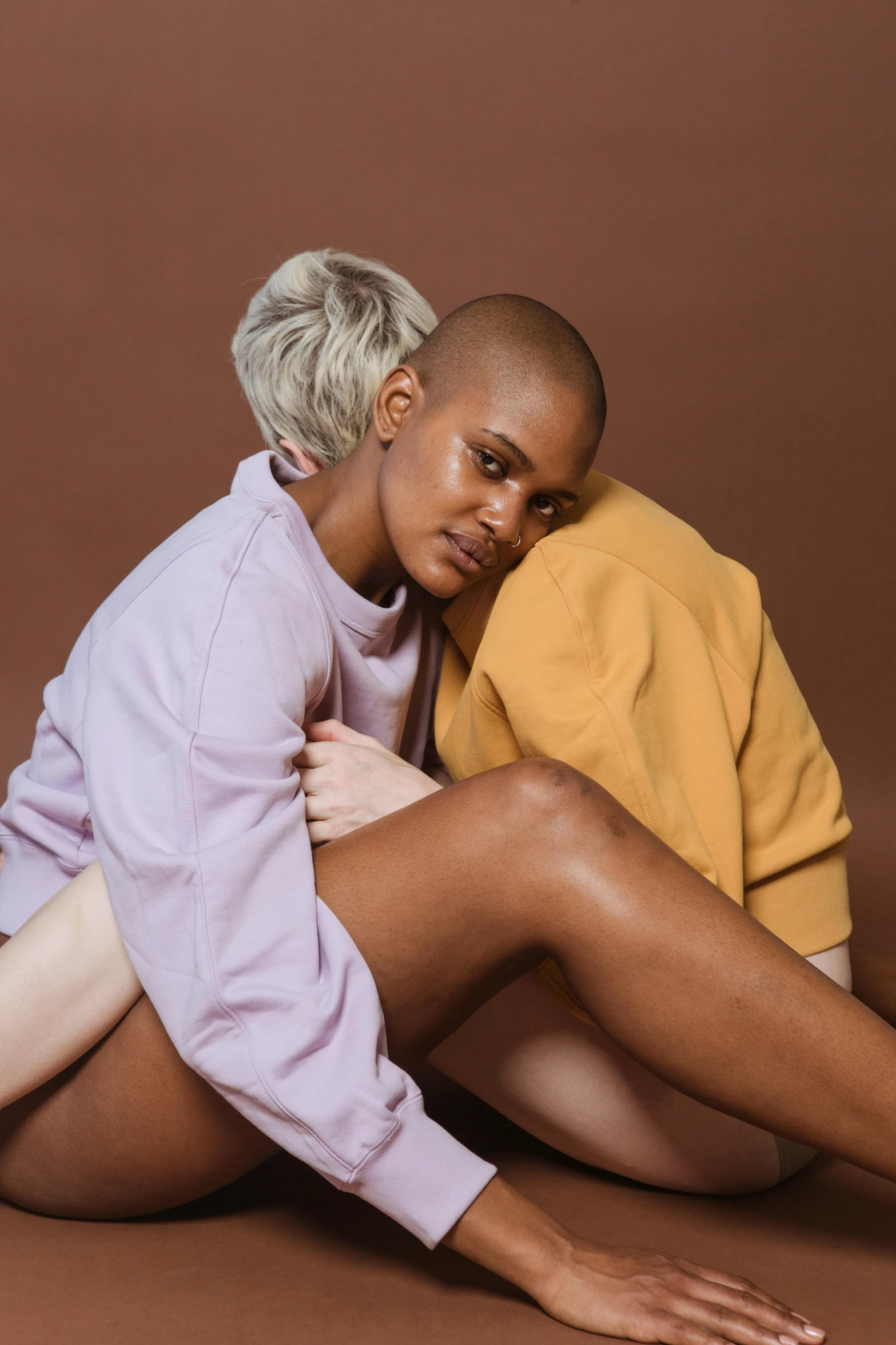 a couple of women sitting next to each other, an album cover, trending on pexels, realism, shaved bald head, brown sweater, lesbian embrace, pastel clothing