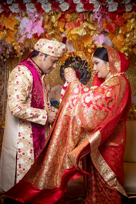 a man and a woman standing next to each other, red and gold cloth, bangladesh, bride and groom, looking left